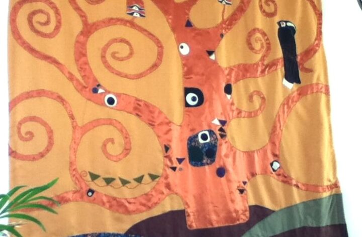 Wandkleed voorstellende een levensboom, gebaseerd op de Stocletfries van Gustav Klimt. De boom is van koperkleurige gladde polyester satijn en staat in golvende heuvels van katoen met een bloemtjesprint en bruine linnen die de aarde voorstellen. De boom heeft taken die zich opkrullen tot spiraalvormen. Op de stam en de taken zitten opgenaaide ogen van katoen en vilt en knopen. In één van de takken zit een zwart-witte gestileerde vogel van vilt.